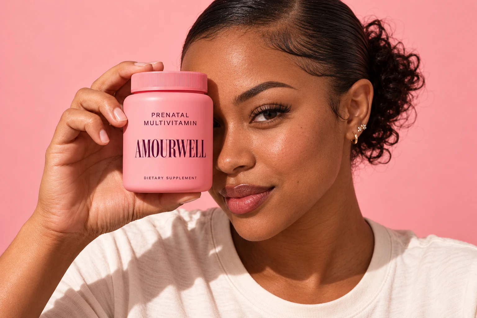 Woman holding a pink Amourwell prenatal bottle over one eye against a pink backdrop